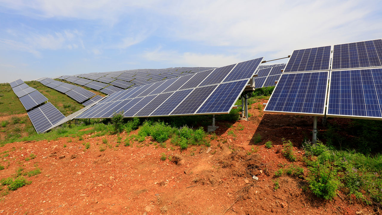 Solar panels placed atop red dirt under clear skies